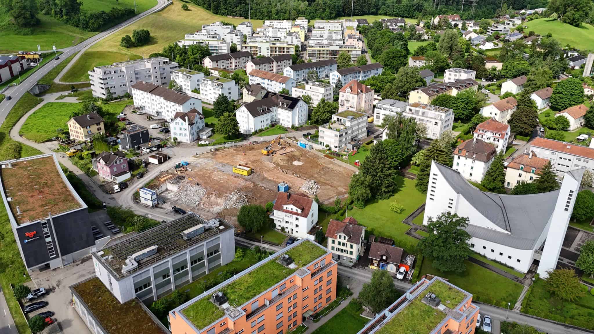 Vacant construction site in a suburban neighborhood surrounded by residential buildings and green spaces.
