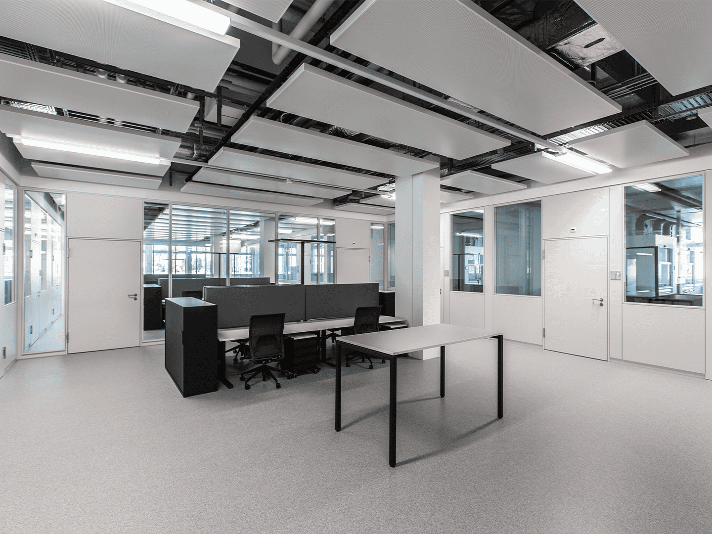 Modern minimalist office space with white walls, black chairs, glass partitions, and an acoustic ceiling design in a professional corporate environment.
