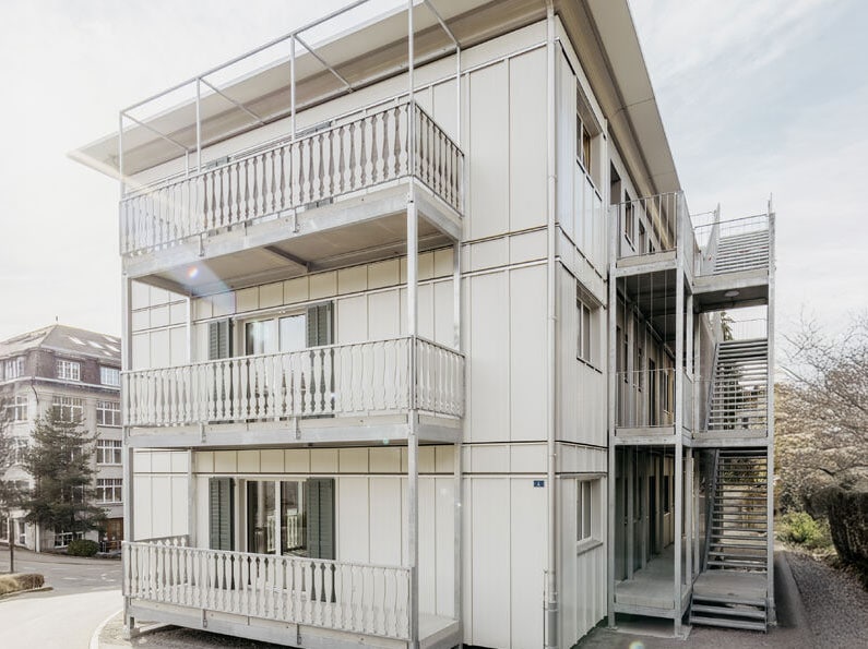 Open metal staircase on the exterior of a modern apartment building with balconies and multiple floors in an urban setting.