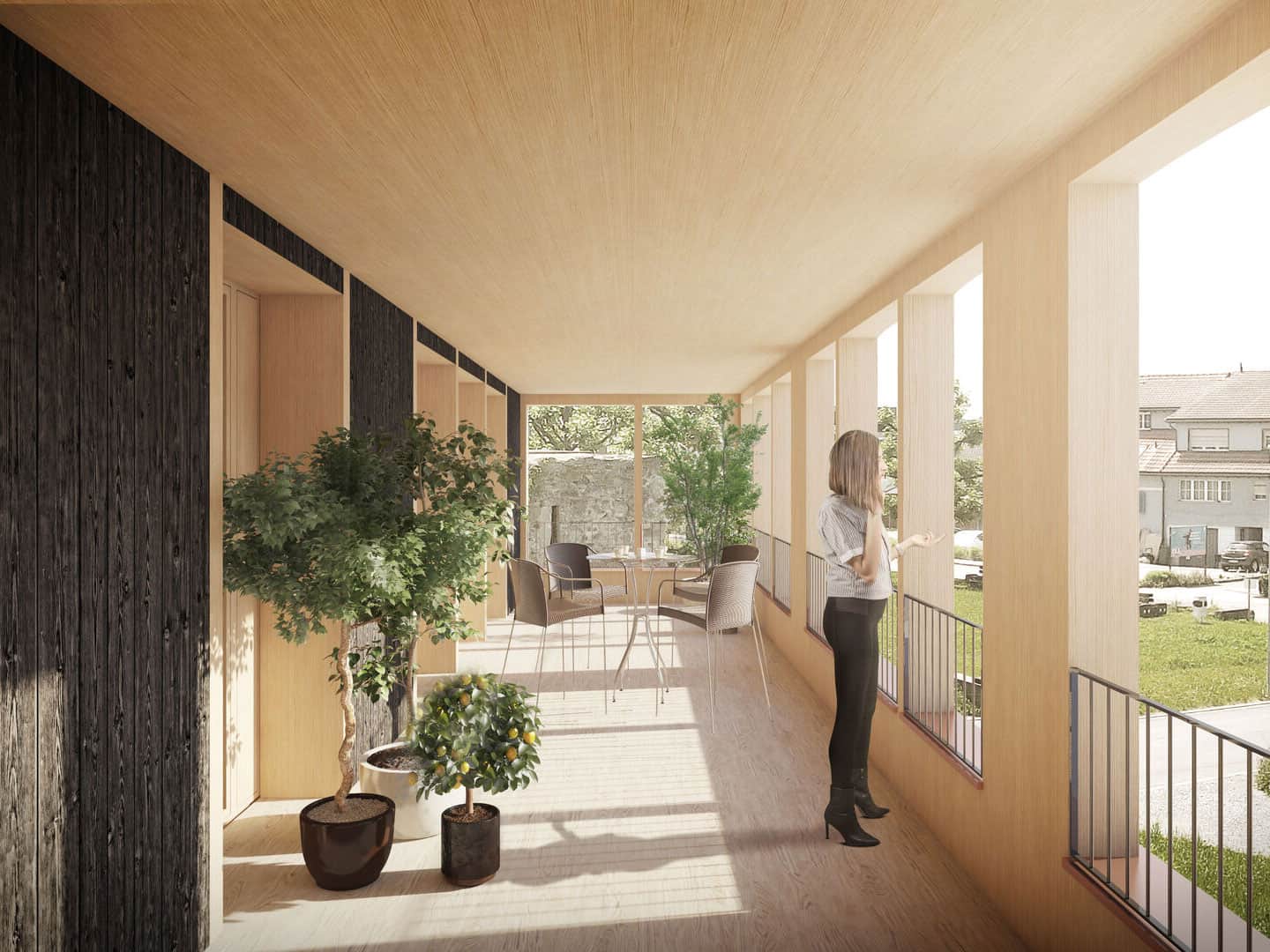 Brightly lit balcony with large windows, wooden floors, and potted plants, featuring a woman talking on the phone and a dining area, surrounded by greenery and neighboring buildings.