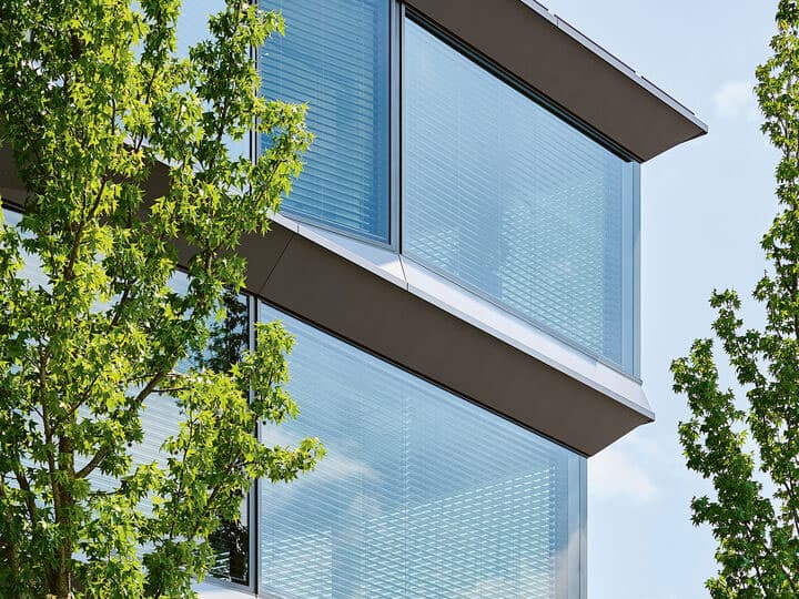 Modern glass building with sleek, reflective windows and surrounding green trees.