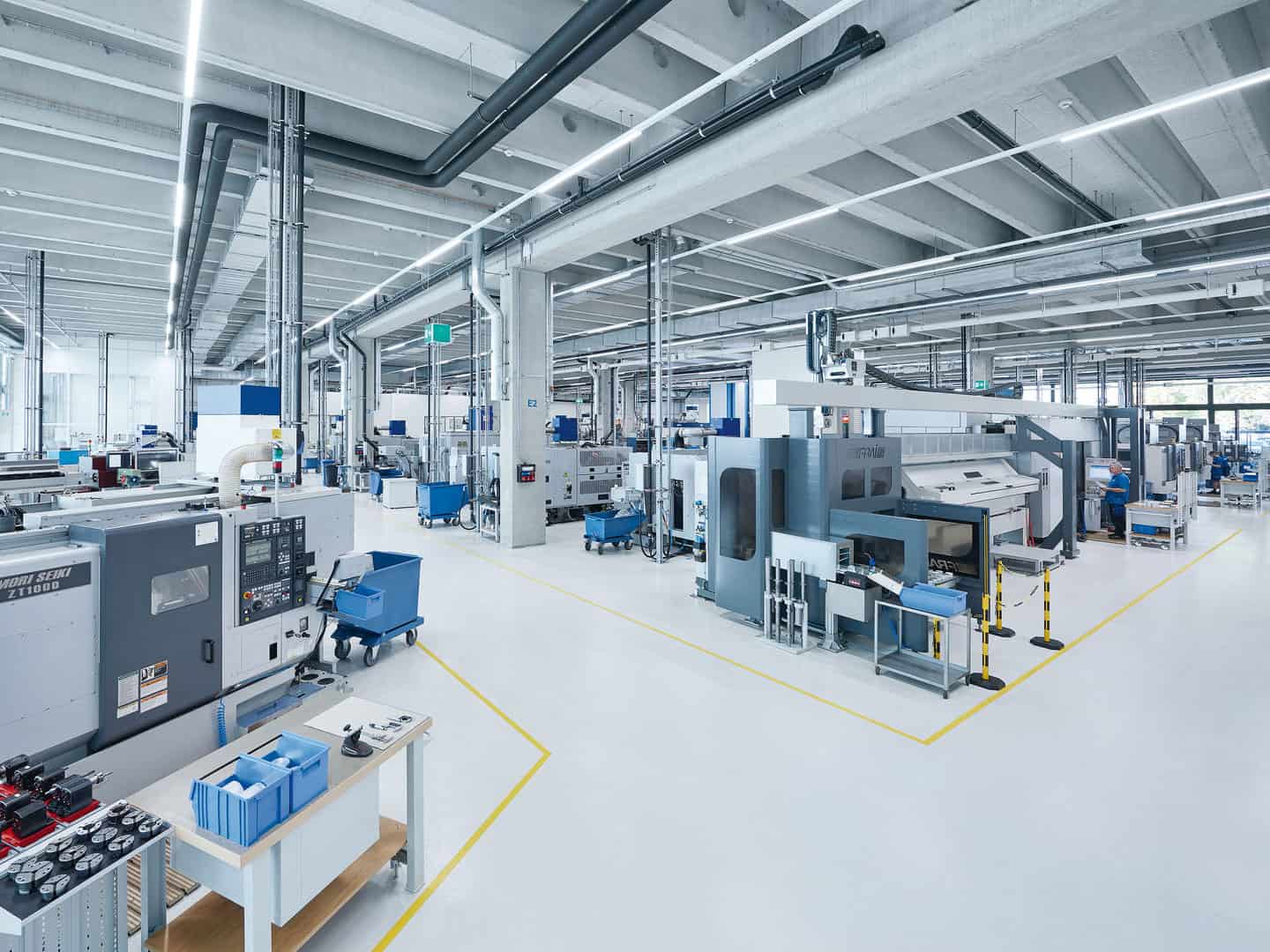 High-tech manufacturing factory with modern machinery, clean environment, and industrial automation systems. Workers are overseeing advanced production lines in a spacious, well-lit industrial setting.