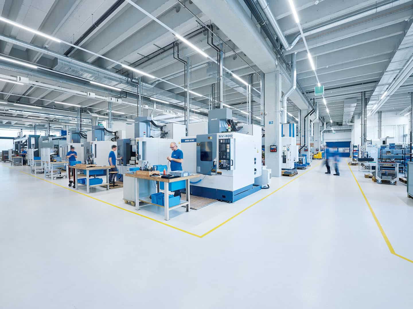 High-tech manufacturing factory with multiple CNC machines, workers in blue uniforms, and a modern, clean industrial environment. Bright lighting and organized workspace promote efficiency.