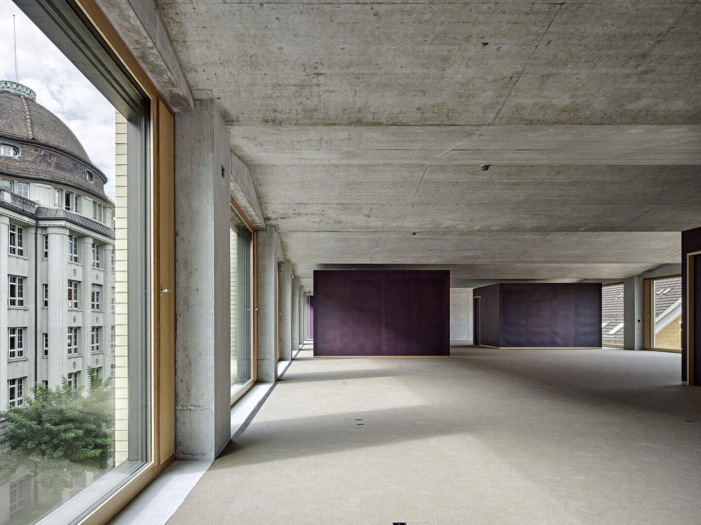 Minimalist modern interior with large windows, exposed concrete ceilings, and dark accent walls in an unfinished building or apartment.