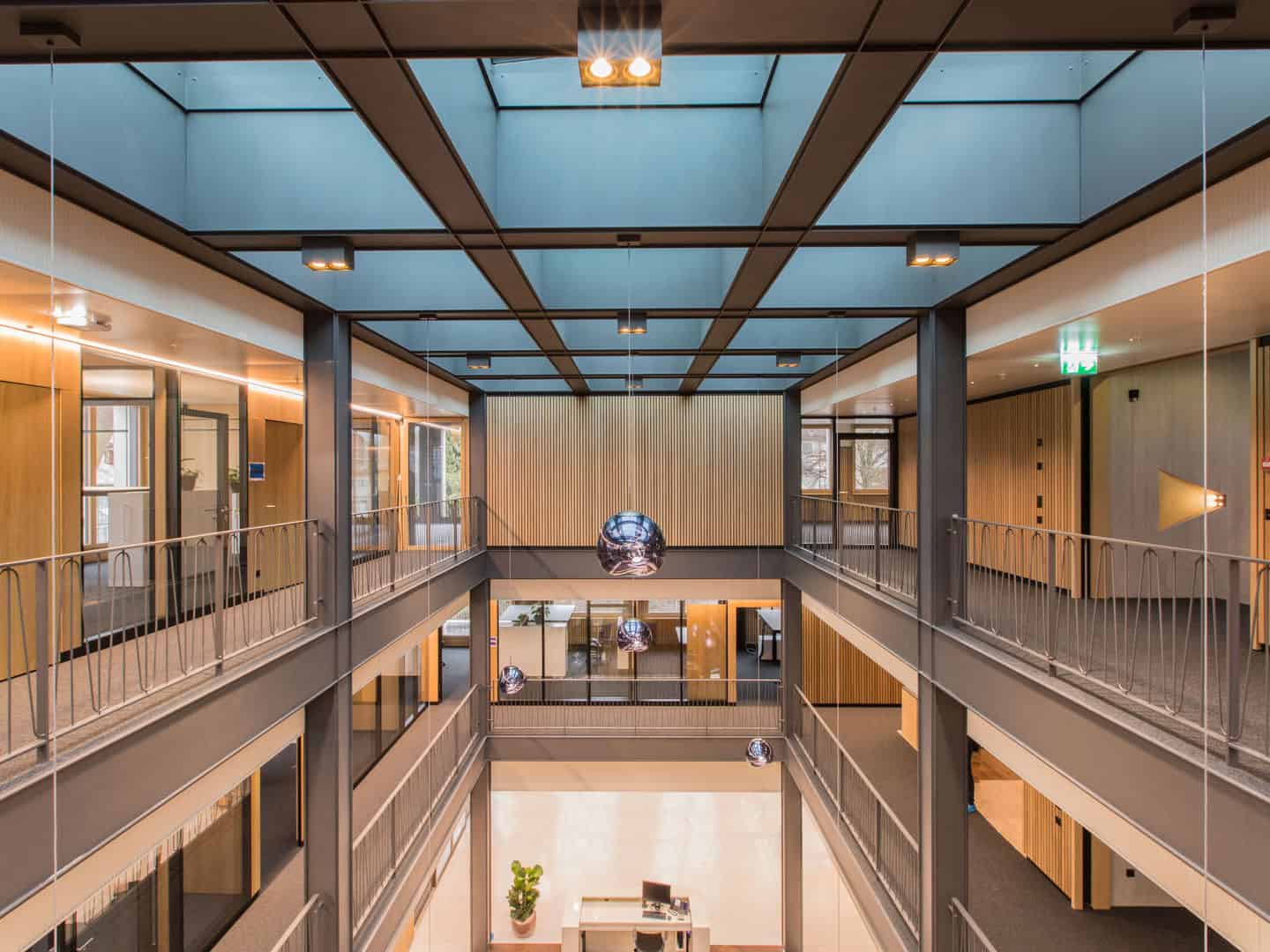 Bright modern office interior featuring multiple levels, large windows, wood accents, and contemporary lighting fixtures creating an open and inviting workspace environment.