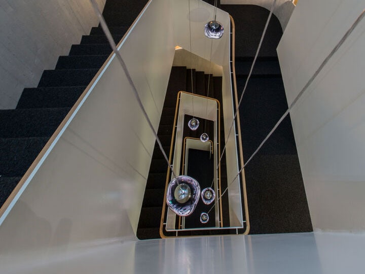 Overhead view of a modern staircase with black steps, white walls, and hanging glass orbs, creating a sleek and contemporary aesthetic.