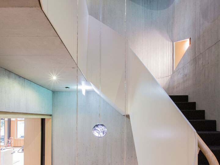 Modern interior staircase with sleek white curves and minimalist design, featuring hanging pendant lights and concrete walls.