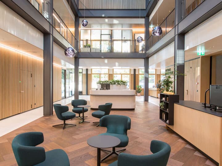 Modern corporate lobby with comfortable seating, natural lighting, and contemporary decor. The space features wood paneling, stylish chairs, and indoor plants for a welcoming atmosphere.