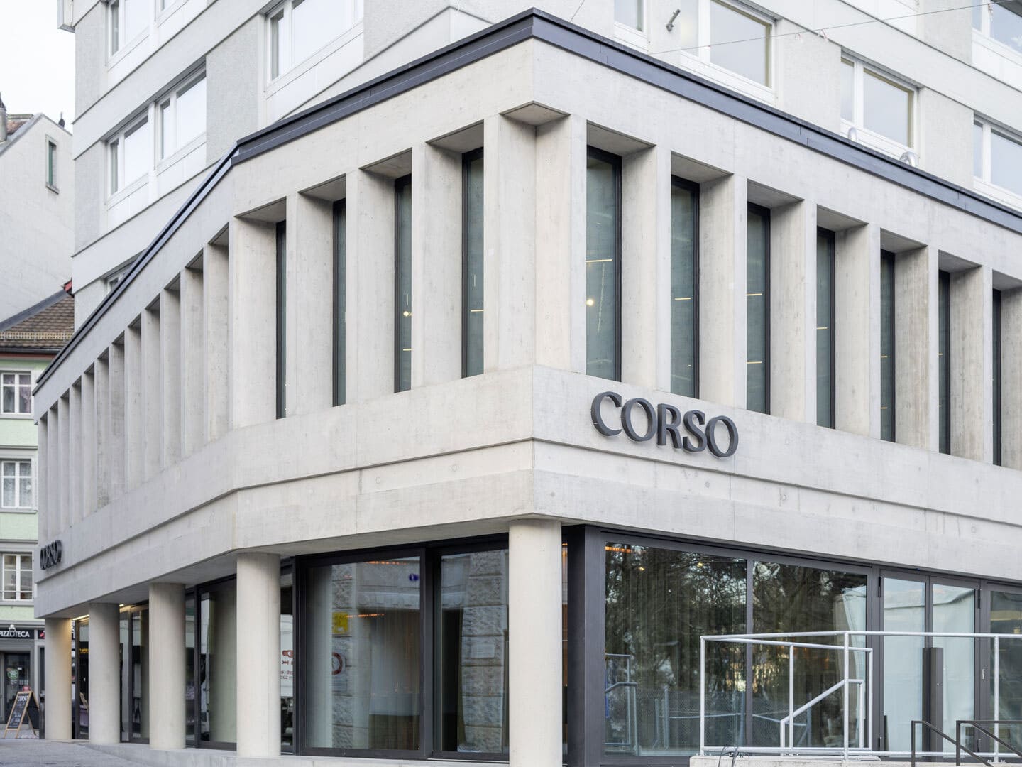 Modern building facade with large vertical windows and the word "CORSO" displayed on the corner, showcasing contemporary architectural design and urban setting.