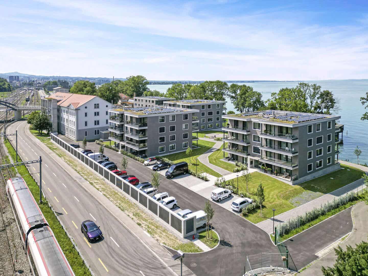 Modern residential apartments near a lake with green lawns and parking area.
