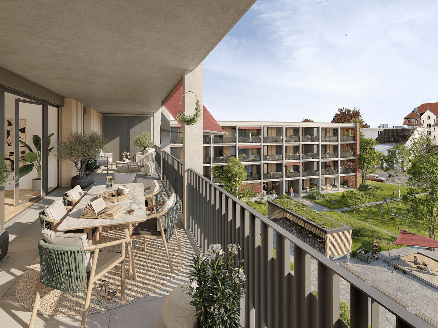 Modern apartment balcony with outdoor furniture and greenery overlooking a residential courtyard and garden during daytime.