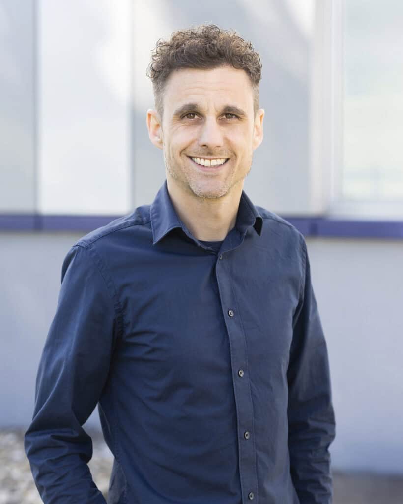 Friendly professional man smiling outdoors in casual navy blue shirt against modern building background.